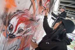 Herakut kreiert eine Wandgestaltung auf dem Lollapalooza Festival, die eine emotionale und surrealistische Figur in leuchtenden Farben darstellt.