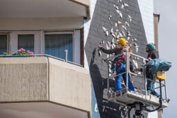 MAdemoiselle Maurice arbeitet mit einer Hebebühne an ihrer Fassadengestaltung mit dreidimensionalen geometrischen Elementen.
