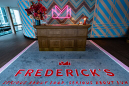 Empfangsbereich im Fredericks Berlin mit Neon-Logo, Mosaikwand und blauem Grafikmuster an den Wänden.