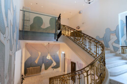 Treppenhaus im Fredericks Berlin mit großflächiger Wandkunst von Daan Botlek und geschwungenem Geländer über zwei Ebenen.