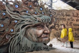 Kinder betrachten ein monumentales Kunstwerk von Herakut mit Naturmotiv und Schriftzügen bei der Urban Nation Biennale