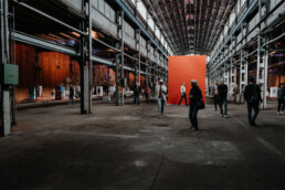 Weitläufige Ausstellungshalle mit Installationen, Wandarbeiten und Besuchern beim Monumenta Festival Leipzig 2018.