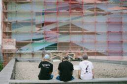 Kera und Team sitzen auf dem Dach und blicken auf die eingeruestete Fassade waehrend der Mural-Produktion von Kera am MWG Forum in Magdeburg.