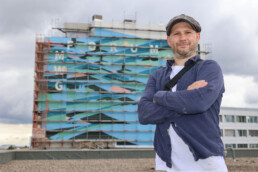 Portrait von Kera vor der eingeruesteten Fassade des MWG Forum