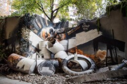 Großformatige Installation von Nomad Clan aus Fässern, Reifen und Wandmalerei im Außenbereich der Urban Nation Biennale