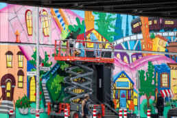 Lady Pink und Team arbeiten auf der Hubarbeitsbühne an der bemalten URBAN NATION Museumsfassade für „Love Letters to the City“.