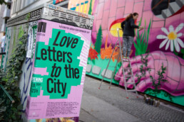 Plakat „Love Letters to the City“ am URBAN NATION Museum, im Hintergrund arbeitet Lady Pink am Fassadenmural