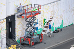 WIP an der URBAN NATION Museumsfassade: Skizzenlinien und erste Farbflächen bei der Produktion von „Love Letters to the City“ (Lady Pink).