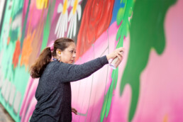 Lady Pink sprayt eine grüne Form auf der farbigen Museumsfassade – Detailaufnahme aus der WIP-Produktion zu „Love Letters to the City“.