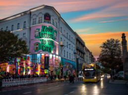 URBAN NATION Museumsfassade mit „Love Letters to the City“ und farbigem City-Motiv von Lady Pink bei Abendlicht.