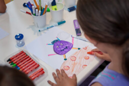 Kind malt eine Monsterzeichnung am Tisch – Urban Nation Monster Project Workshop.