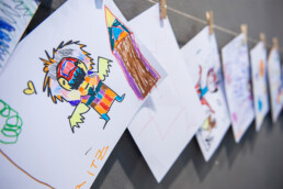 Kinderzeichnungen hängen an einer Leine als Mini-Ausstellung beim Urban Nation Monster Project Workshop.