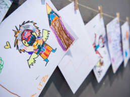 Kinderzeichnungen hängen an einer Leine als Mini-Ausstellung beim Urban Nation Monster Project Workshop.