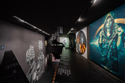 Ausstellungsraum im Obergeschoss des Urban Nation Museums mit großem Porträt-Kunstwerk und weiteren Wandarbeiten