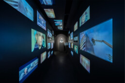 Dunkler Ausstellungsraum im Obergeschoss des Urban Nation Museums mit mehreren leuchtenden Bildschirmen an den Wänden