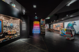 Weitwinkelblick im Untergeschoss des Urban Nation Museums mit Installationen und farbig beleuchteter Treppe im Hintergrund