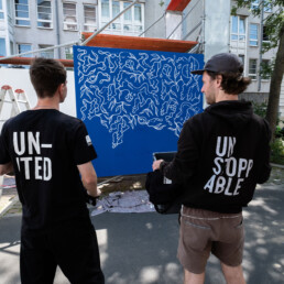 yap studio crew und LEITI stehen vor seiner blauen Kunstwand beim Urban Nation Open-Air zur Ausstellung „Talking and other banana skins