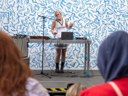 Live-Musik-Performance von Cile vor blauem Line-Art-Wandbild von LEITI beim UN-ARTig zur URBAN NATION Ausstellung „Talking and other banana skins“