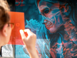 Besucherin hält Rotfilter vor ein 3D-Mural von Insane51 mit cyan-rotem Doppelmotiv