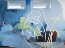 Abstrakte Wandgestaltung im Treppenaufgang des Vienna House Easy by Wyndham Berlin am Potsdamer Platz &ndash; Kunstwerk von Johannes Mundinger in Blau- und Gr&uuml;nt&ouml;nen mit linearen Formen entlang des Gel&auml;nders.