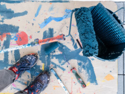 Arbeitsmaterialien bei der Produktion des Waterkant Murals: Farbrolle, Eimer und Malwerkzeuge auf farbverschmierter Schutzpappe – Kunstwerk von Stohead.