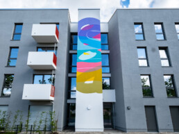 Außenansicht des Gebäudes mit vertikaler Fassadengestaltung des Waterkant Murals – Kunstwerk von Stohead.