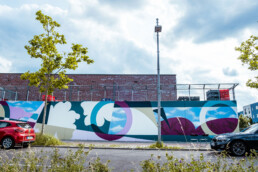 Gesamtansicht der 40 m Wandgestaltung für ANH Hausbesitz entlang der Strasse, abstraktes Farbkonzept mit Himmelblau-Elementen.