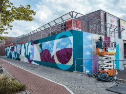 Gesamtansicht der 40 m Wandgestaltung für ANH Hausbesitz, Hebebühne im Einsatz während der Umsetzung.