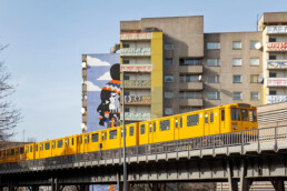Brave Wall: Gesamtansicht des fertigen Murals von Kate Voronina an einem Hochhaus, gelbe U-Bahn fährt vorbei.