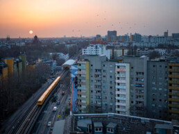 Brave Wall: Stadtblick bei Sonnenuntergang mit Voronina-Mural am Hochhaus entlang der U-Bahn-Trasse.