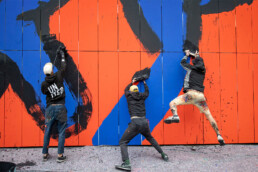 Actionaufnahme bei der Fassadenmalerei: Broken Fingaz Crew arbeiten an schwarzen Formen auf blau-orangen Flächen der Museumsfassade
