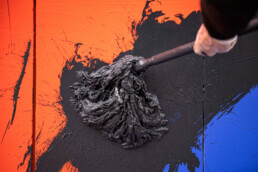 Detailaufnahme: schwarzer Farbauftrag mit Mop auf orange-blauem Hintergrund der Broken Fingaz Crew Fassadengestaltung