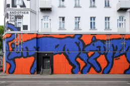 Frontale Detailansicht der fertigen blau-orangen Fassadengestaltung mit schwarzer Linienführung und Typografie am URBAN NATION Museum