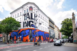 Fertige Museumsfassade von Broken Fingaz Crew am URBAN NATION Museum mit großformatiger Typografie und blau-orangen Flächen