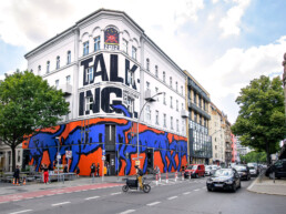 Fertige Museumsfassade von Broken Fingaz Crew am URBAN NATION Museum mit großformatiger Typografie und blau-orangen Flächen