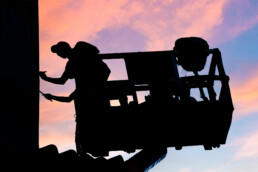 Silhouette eines Künstlers auf der Hebebühne vor Abendhimmel während der Fassadenproduktion am URBAN NATION Museum