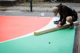 Detailarbeit am Spielfeld: saubere Farbkante und Abklebung, Person richtet die Linie am Rand einer Farbfläche aus.