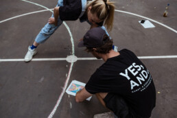 Planung auf dem Asphalt: Skizze/Referenzblatt liegt auf dem Court, zwei Personen stimmen die Geometrie und Linienführung ab.