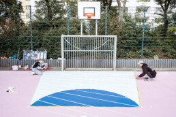 Umsetzung des „Hypercourt“: zwei Personen arbeiten am Spielfeld unter dem Basketballkorb, Linien werden abgeklebt und vorbereitet.