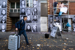 Passant mit Rollkoffer vor großformatiger Inside Out Porträt-Fotowand, daneben Gerüst mit Montagearbeiten in Berlin.