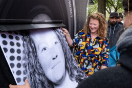 Person zieht ein frisch gedrucktes Schwarzweiß-Porträtposter aus dem Photo-Booth-Truck beim Inside Out Projekt in Berlin.