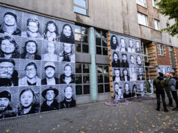 Großflächige Inside Out Porträtwände an einer Gebäudefassade, mehrere Personen betrachten die Montage vor Ort in Berlin.