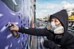 Lady Aiko sprayt Details am Fassadenmural der Urban Nation Museum Fassade, inspiriert von Motiven von Martha Cooper.
