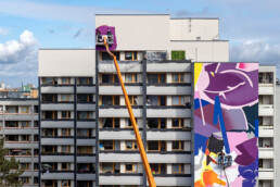 One Wall Produktion: SatOne arbeitet mit Hebebühne an abstraktem Mural in Violett und Pink, Urban Nation