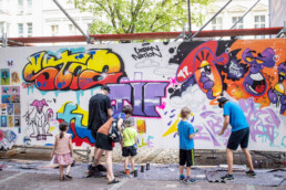 Kinder und Erwachsene gestalten gemeinsam eine Graffiti-Wand mit Figuren und Lettering beim UN-ARTIG Festival.