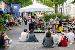 Liveband auf einer kleinen Open-Air-Bühne, Publikum sitzt und steht davor beim UN-ARTIG Festival.