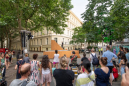 Zuschauer vor einer erhöhten Holzbühne mit Performance und Lichttechnik beim UN-ARTIG Festival.