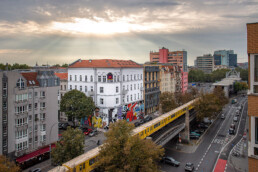Weitwinkel-Umfeldansicht mit Urban Nation Museum Fassade und Mural von Lady Aiko im Stadtraum.