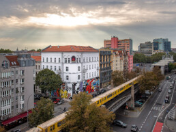 Weitwinkel-Umfeldansicht mit Urban Nation Museum Fassade und Mural von Lady Aiko im Stadtraum.
