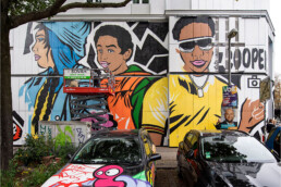 Fassadenmural von Lady Aiko an der Urban Nation Museum Fassade mit großformatigen Figuren und Hebebühne vor Ort.